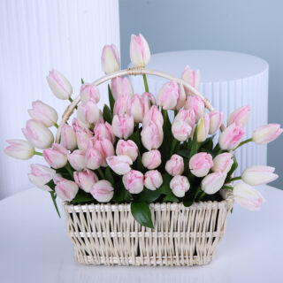 A charming basket of delicate light pink tulips, beautifully displayed on a white round table.