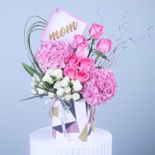 Stylish floral arrangement with pastel pink hydrangeas and roses, displayed in a chic gift box with "Mom" sign