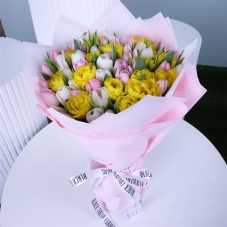 A large bouquet of tulips in pink, white, and yellow, wrapped in light pink paper and tied with a white ribbon