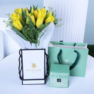 Yellow tulips floral box in a white wrap, presented with a gift bag of Patchi chcolates.
