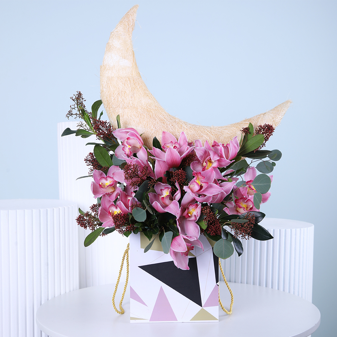 Pink orchid arrangement with a decorative crescent moon, presented in a modern geometric box.