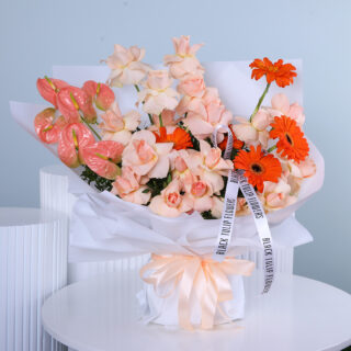 A bouquet featuring peach roses, orange gerberas, and anthuriums in a white wrap with a peach ribbon.