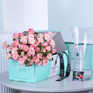 10 pink baby roses in a gift box with a glass vase and flower food, displayed on a table.