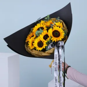 A bouquet of bright yellow sunflowers wrapped in black and tan paper.