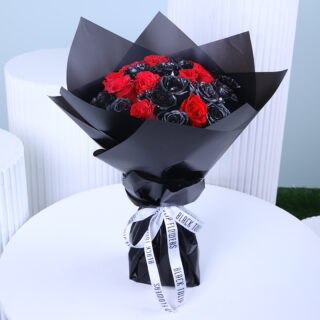 A bouquet featuring deep black roses, elegantly paired with green ruscus leaves, wrapped in pristine white, and tied with a white satin ribbon.