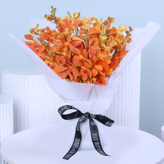 A hand-tied bouquet of vibrant orange mokara orchids wrapped in white paper and finished with a black ribbon.