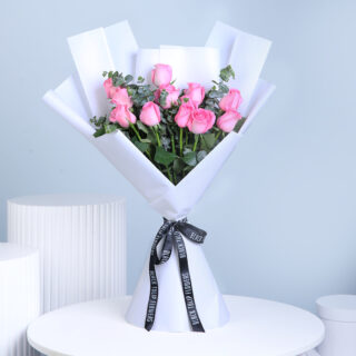 A wrapped bouquet containing 12 pastel pink roses and green eucalyptus, tied with a black ribbon.