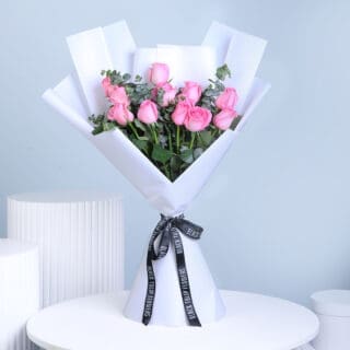 A wrapped bouquet containing 12 pastel pink roses and green eucalyptus, tied with a black ribbon.