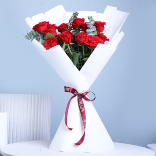 A bouquet containing 12 vibrant red roses with green eucalyptus, wrapped in white and secured with a dark red ribbon.