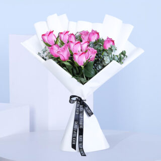 A beautifully arranged bouquet of a dozen vibrant purple roses with green leaves, wrapped in white.