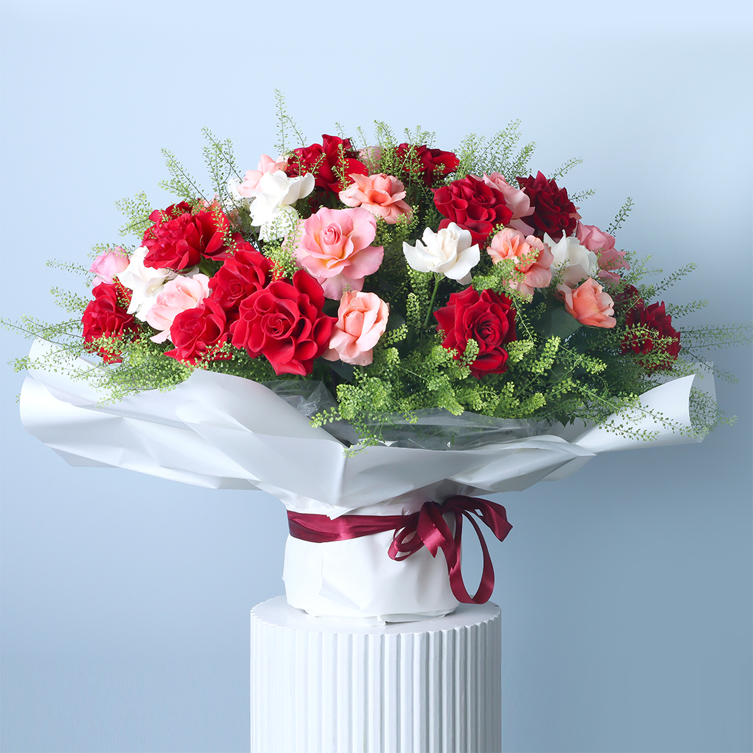 A vibrant bouquet featuring a mix of red, pink, and white roses accented with delicate white lepidium, wrapped in white and tied with a burgundy ribbon.