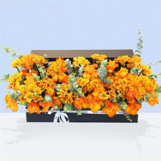 An arrangement of bright orange roses and chrysanthemums, presented in a black rectangular box with a white ribbon.