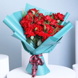 A premium bouquet of deep red roses with green foliage and green wrap, tied with a ribbon, set against a soft blue background.