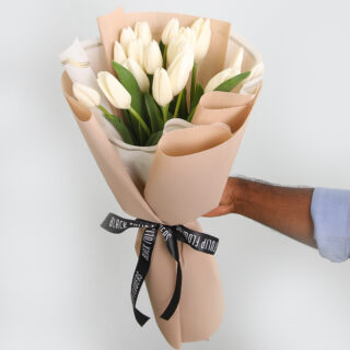 A graceful bouquet of pure white tulips wrapped in light brown and tied with a black ribbon,