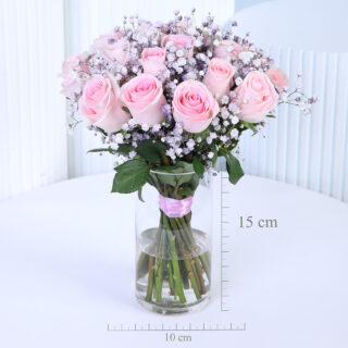 A bouquet of about 20 dark pink roses, surrounded by a cloud of white baby’s breath, is arranged in a clear glass vase with visible green stems tied with pink ribbon.