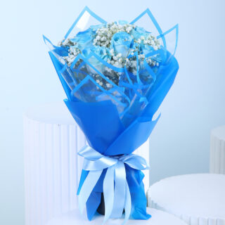 A bouquet of blue roses and white baby's breath, wrapped in blue and clear geometric patterned paper with a light blue and white ribbon.