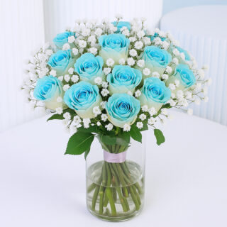 A unique bunch of blue roses with baby’s breath in a clear glass vase tied with a pink ribbon.