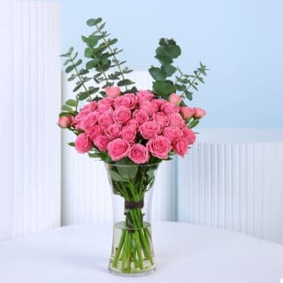A bunch of 20 vibrant pink spray roses in a clear glass vase, with green eucalyptus leaves adding height and contrast.