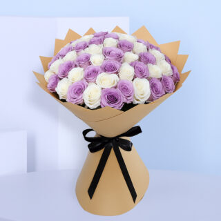 A large bouquet showing alternating layers of pure white roses and light purple roses, creating a serene bi-color effect. The bouquet is wrapped in a light brown paper and tied with a black ribbon.