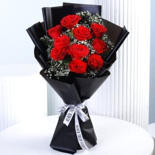 A bouquet of 10 vibrant red roses with white gypsophila (baby's breath) wrapped in black paper and tied with a black and white ribbon.