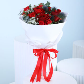 A bouquet of red roses, white baby's breath, and green eucalyptus wrapped in white with a red ribbon.