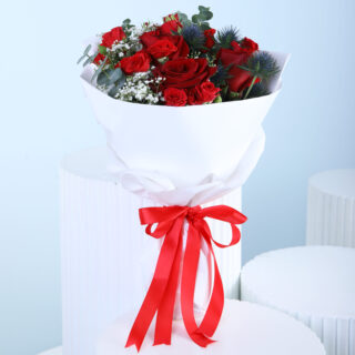 A bouquet of red roses, white baby's breath, and green eucalyptus wrapped in white with a red ribbon.