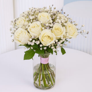 White rose floral arrangement in a glass vase with white baby’s breath tied with a pink ribbon.