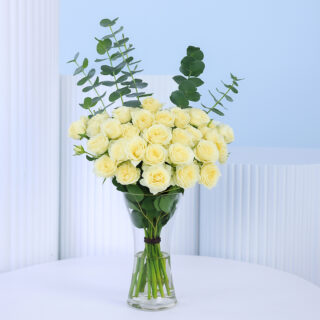 A beautiful bunch of 20 white spray roses in a clear glass vase with eucalyptus leaves.