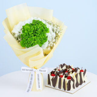 A bouquet of white and green hydrangeas and baby's breath wrapped in light yellow and a square black forest cake