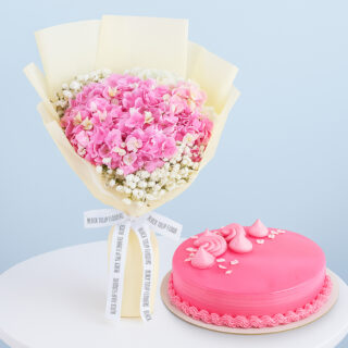 A flower combo featuring a bouquet of pink hydrangeas with baby's breath wrapped in cream and tied with a black and white ribbon with a round pink frosted cake.