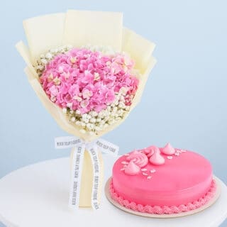 BTF Home 49 A flower combo featuring a bouquet of pink hydrangeas with baby's breath wrapped in cream and tied with a black and white ribbon with a round pink frosted cake.
