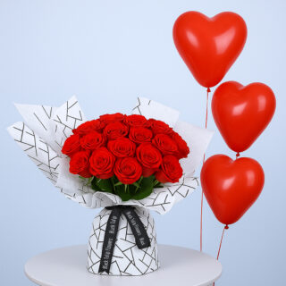 A bouquet of red roses wrapped in black and white geometric patterned paper and tied with a black ribbon and red heart-shaped balloons.