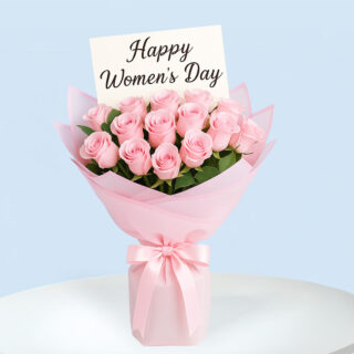 A bouquet of soft pink roses wrapped in layers of light and dark pink paper and tied with a light pink satin ribbon, with a message card that reads "Happy Women's Day".