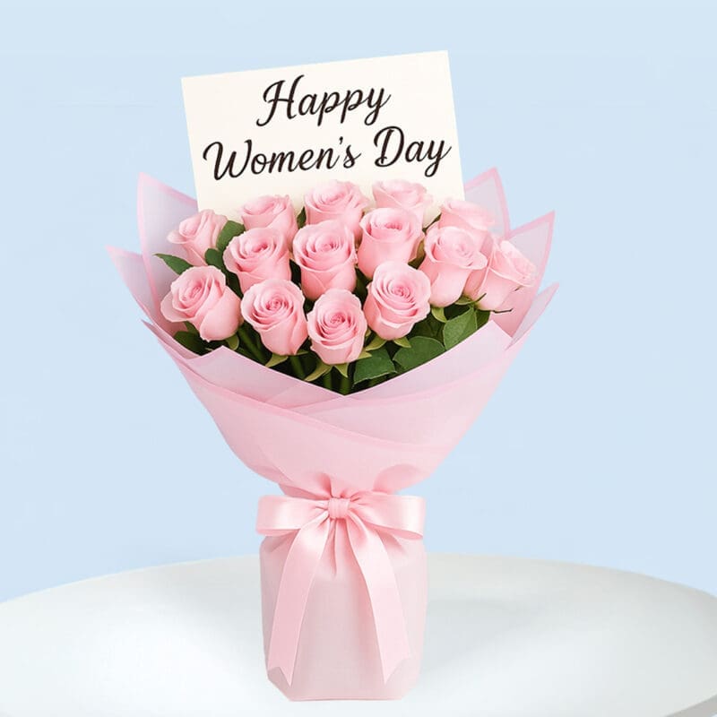 womens-day-rose-bouquet-01 A bouquet of soft pink roses wrapped in layers of light and dark pink paper and tied with a light pink satin ribbon, with a message card that reads "Happy Women's Day".