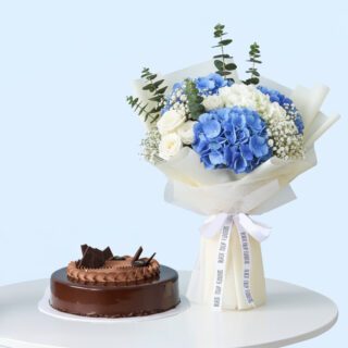 Flower Delivery Abu Dhabi 26 A bouquet featuring blue hydrangeas, white roses, baby's breath, and eucalyptus, wrapped in white and tied with white ribbon. A rich chocolate cake with a glossy glaze and chocolate frosting is adorned with chocolate bits.