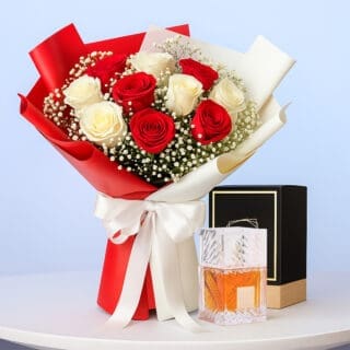 Red and white rose bouquet with baby’s breath in red/ivory wrap with white ribbon, displayed beside a boxed perfume.