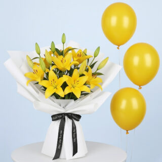 A combo of a vibrant yellow lily bouquet with multiple blooming lilies and green buds, wrapped in white with a black branded ribbon and three shiny yellow balloons.