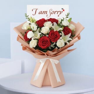 BTF Home 43 I am Sorry bouquet with red and white roses, white lilies, and tanacetum, wrapped in peach paper and tied with a white ribbon.