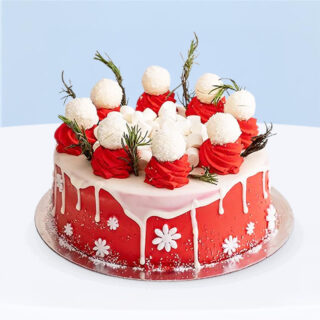 A Christmas-themed red and white cake, topped with white chocolate truffles and festive cream swirls.