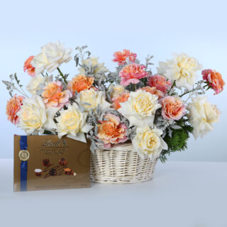 Basket of white and orange Ecuador roses with greenery and Lindt Swiss chocolates.