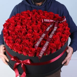 Luxury Valentine flower box featuring 100 red roses arranged in a black round box with red ribbon bow.