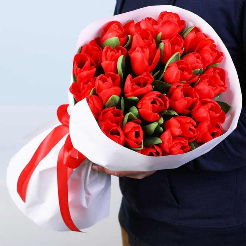 Bouquet of 30 red tulips in a white wrap style, finished with a red ribbon.