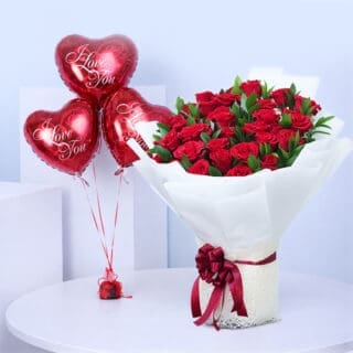Red roses and green foliage in a white wrap, paired with red heart balloons printed “Love You”.
