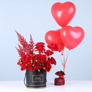 A black box featuring red spray roses and red blooms paired with three red heart balloons.