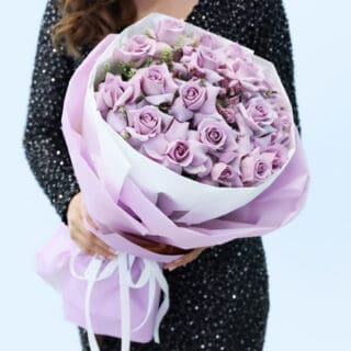 Purple roses with delicate fillers in lilac and white wrapping, finished with a ribbon tie.