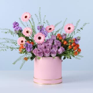 A vibrant floral arrangement featuring pink, purple, and orange blooms styled in a structured pink gift box with a full, colourful presentation.