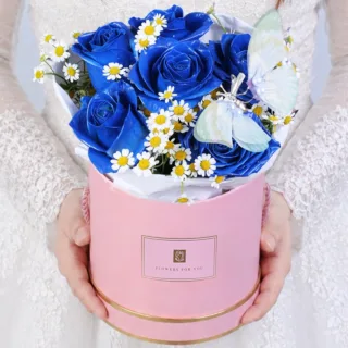 Blue rose box combined with tanacetum blooms and a butterfly accent arranged in a creative and eye-catching floral design.