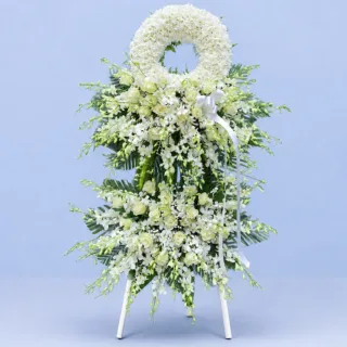 Eternal White Tribute Stand featuring white chrysanthemums, white dendrobium orchids, white roses, gypsophila, palm leaves, and fresh greenery arranged as an elegant sympathy wreath stand.