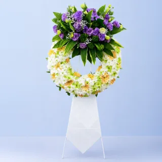 White & Purple Tribute Wreath Stand featuring white chrysanthemums, purple lisianthus, peach gerberas, green chrysanthemums, gypsophila, and fresh greenery arranged on a white steel sympathy wreath stand.