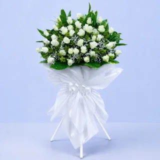 White Rose Tribute Stand featuring 120 white roses, solidaster, gypsophila, cordyline leaves, and fresh greenery elegantly arranged on a white steel sympathy flower stand.